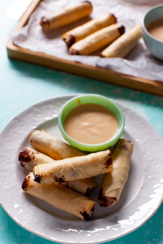cheeseburger egg rolls on white plate with sauce, egg rolls on a tray in background