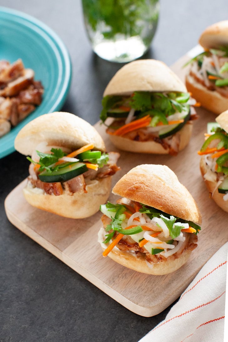 Lemongrass Chicken Banh Mi Sliders from thelittlekitchen.net chicken banh mi sliders on a wooden board with a plate of chicken in the background