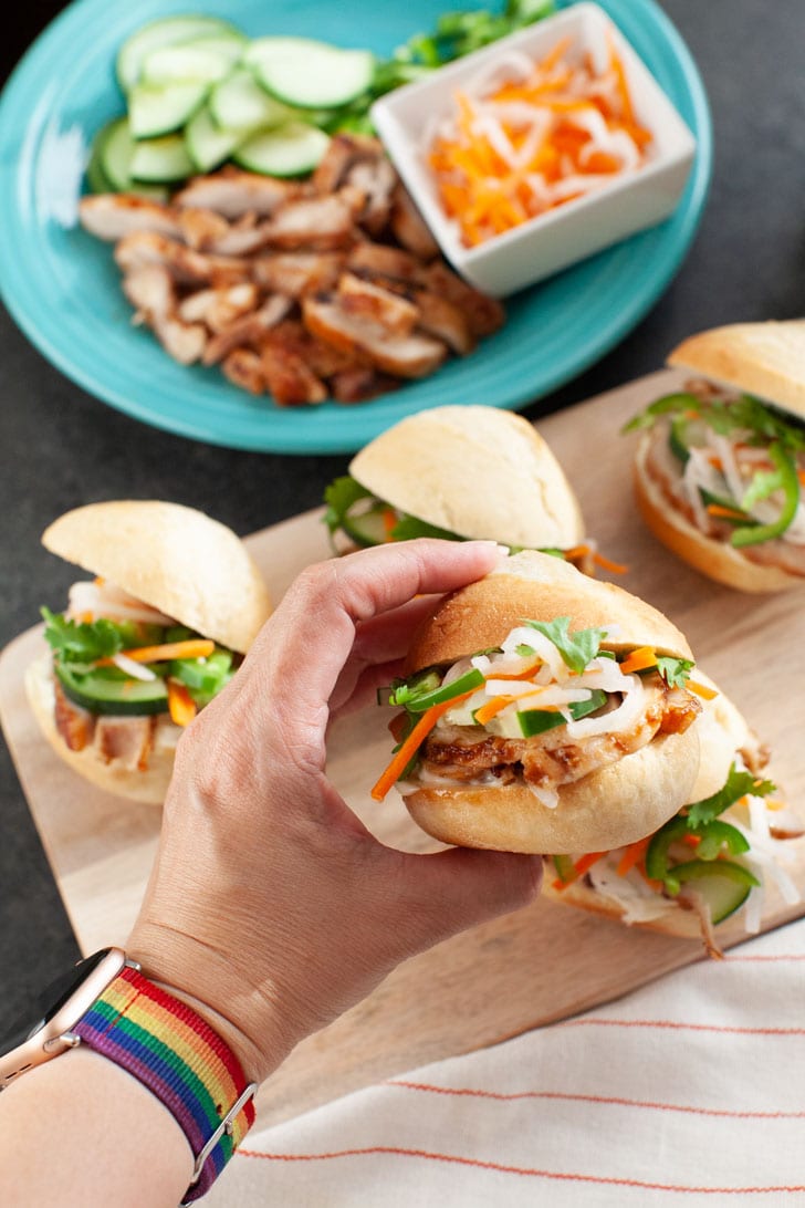 Lemongrass Chicken Banh Mi Sliders from thelittlekitchen.net a hand holding one banh mi slider with a few other chicken banh mi sliders on a wooden board