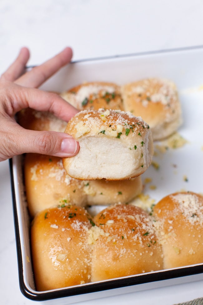 Parmesan Garlic Rolls from thelittlekitchen.net a hand holding a parmesan garlic roll with garlic rolls in a baking dish in the background
