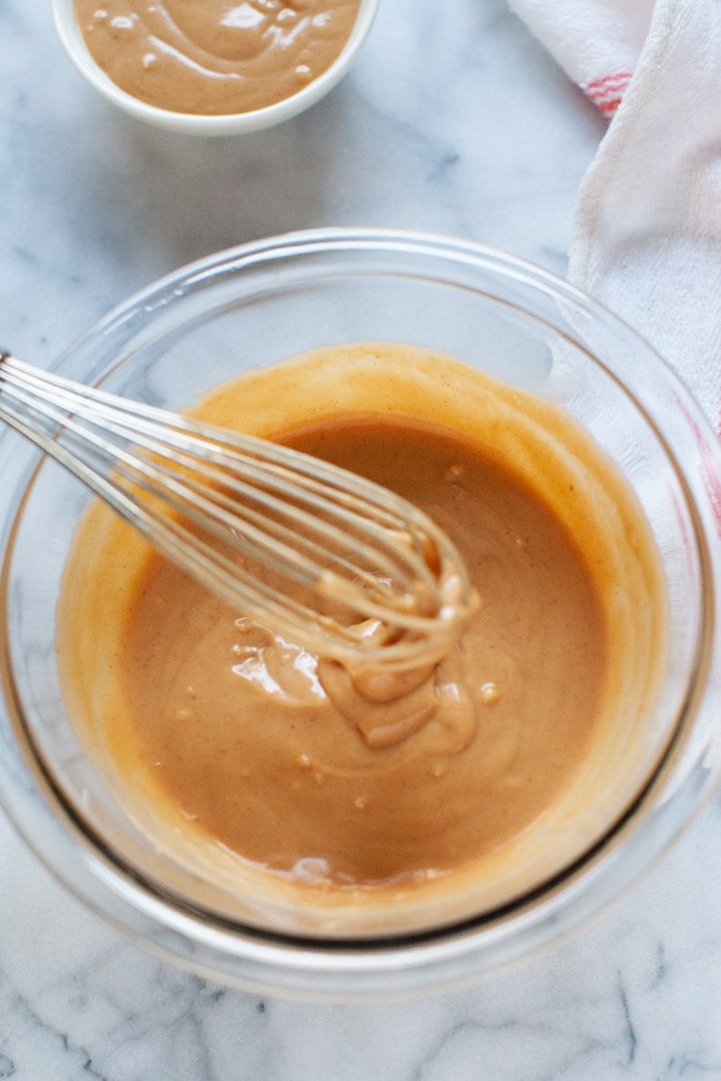 Peanut Sauce from thelittlekitchen.net peanut sauce in a glass bowl with a whisk over the bowl