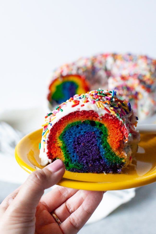 Rainbow Bundt Cake from thelittlekitchen.net Slice of rainbow cake on a plate with the full cake in the background