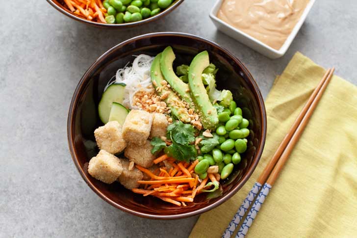 Tofu Bowl from thelittlekitchen.net brown bowl with tofu, noodles, edamame, carrots and avocado and chopsticks on top of a napkin