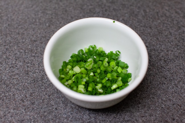Vegetarian Dumplings from thelittlekitchen.net Small white bowl on gray countertop filled with thinly sliced green onions Vegetarian Dumplings from thelittlekitchen.net